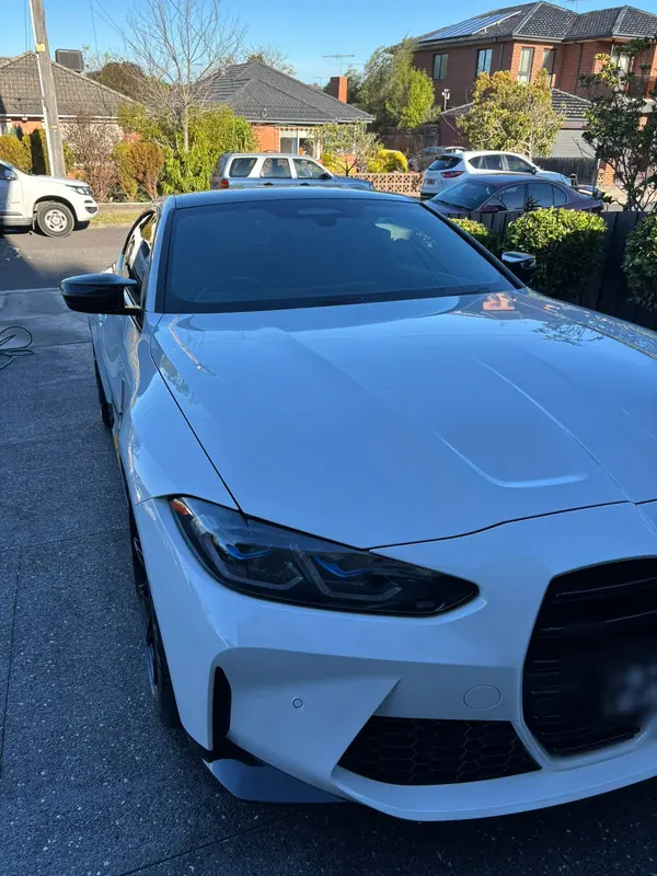Front three-quarter view of the white M4 with the bonnet reflecting the sky