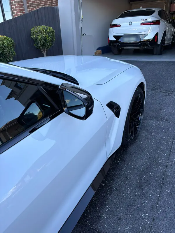 Mirror and front guard of the white M4, with an X4 M parked in the garage