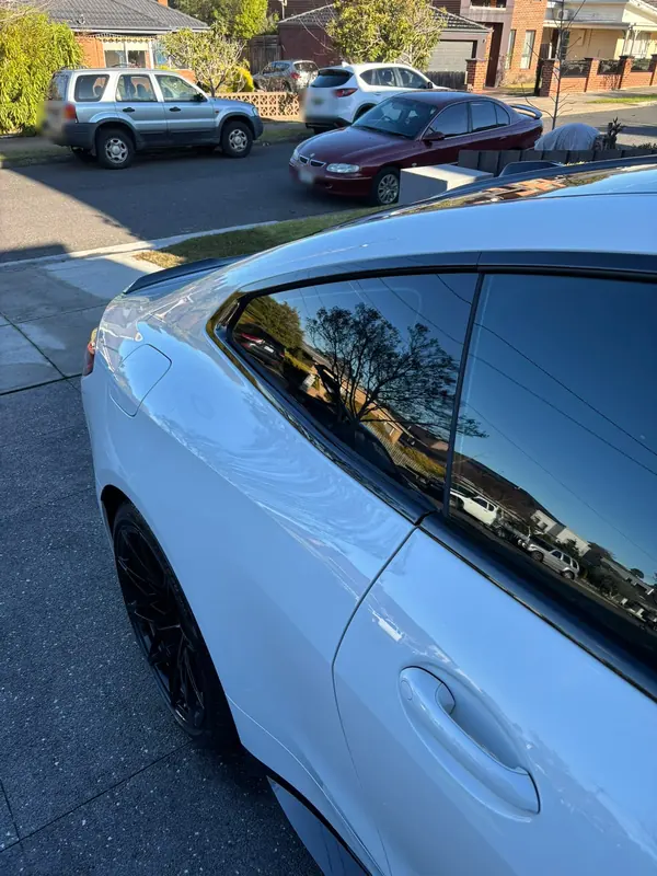 Rear quarter of the white M4 with trees reflected in the window