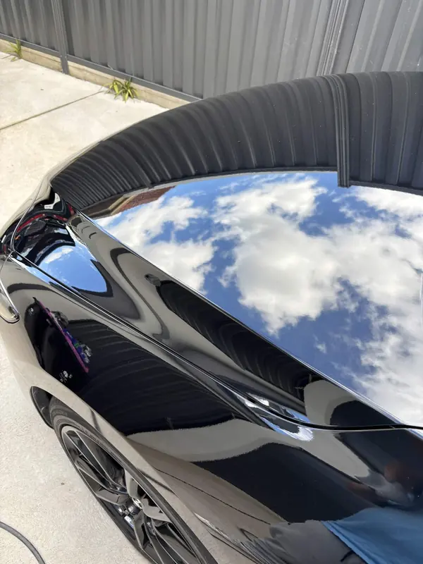 Roof spoiler and hatch of the black Mazda 3 reflecting clouds