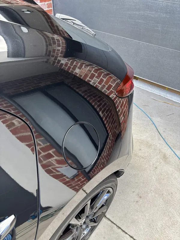 Side of the black Mazda 3 reflecting a brick wall